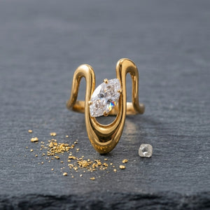 Gold ring with marquise-cut stone on slate surface, next to loose stone and gold flakes