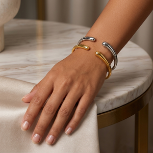 Gold and silver metal cuff bracelets on wrist, marble tabletop background