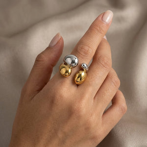 Steel and gold-tone pebble ring on a hand with a neutral background