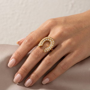 Gold horseshoe ring adorned with small gems on hand resting on fabric