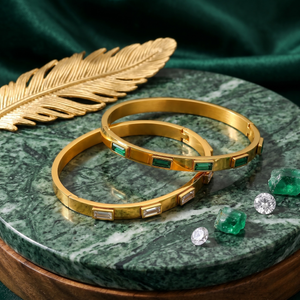 Gold bangle set with emerald and diamond accents on green marble surface with gold leaf decor.