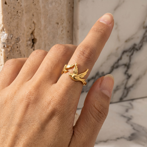 Gold ring with foliage design on model's finger against marble background