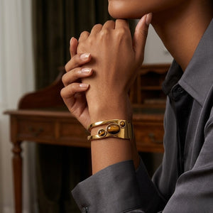 Gold bracelet with earth tone stones on a model's wrist against a sophisticated indoor setting