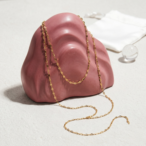 Gold Y-Link Chain displayed on a pink sculptural stand in a minimalist setting