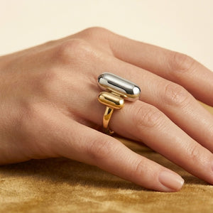 Tonal Fusion Ring in silver and gold on hand, showcasing modern dual-metal capsule design on soft fabric background.