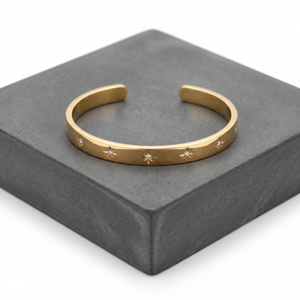 Gold cuff bracelet engraved with starburst design on a gray background