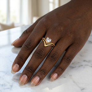 Chevron Facet Ring in gold on hand, features a central heart-shaped diamond, on a marble surface.