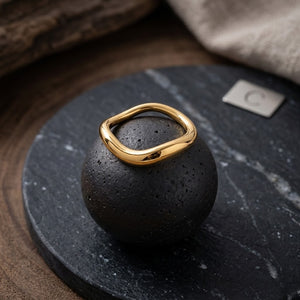 Gold wave band ring on black stone display, J.Collins Jewelry