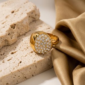 Gold dome ring with sparkling diamonds on a textured stone background and draped gold fabric