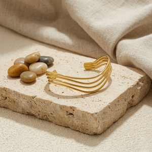 Layered hollow gold bangle on stone slab with pebbles and linen fabric background