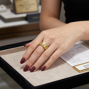 Gold pearl ring with intricate design on a hand with maroon nails in a jewelry display setting.