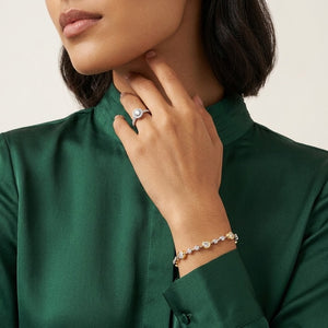 Two-tone gold and sterling silver station bracelet set with bezel-set round cubic Moissanite crystals worn on wrist with matching ring by model wearing an emerald green blouse by J.Collins