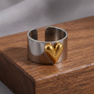 Silver band ring with gold heart accent displayed on a wooden surface