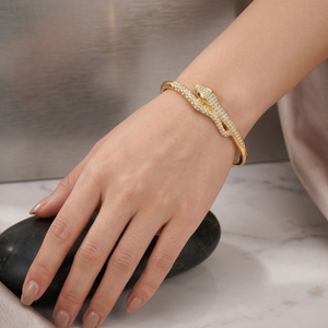 Gold sculptural snake open cuff adorned with crystals on a woman's wrist, hand resting on a dark stone.