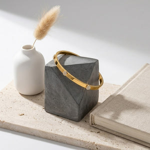 Gold Horizon Beam Bracelet on geometric concrete stand with book and vase for elegant display