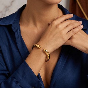 Gold cuff bracelet on a model's wrist, styled with a blue shirt, showcasing elegant, minimalist design.