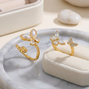 Gold butterfly bypass ring with pearl and crystal accents displayed on a marble and fabric surface.