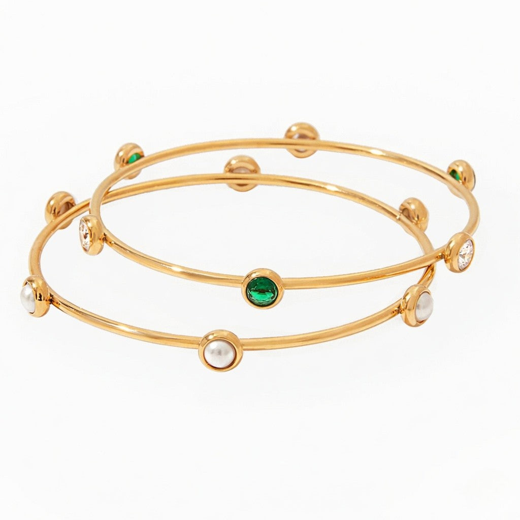 Gold bangles with pearls and emeralds on a white background