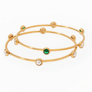 Gold bangles with pearls and emeralds on a white background