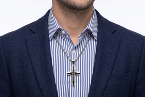 Man wearing a silver crucifix pendant necklace over a striped shirt and blazer