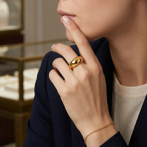 Gold dome ring worn on woman's finger with blue blazer, jewelry store setting in background
