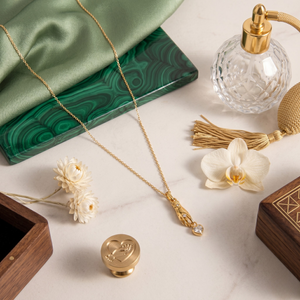 Gold heart stone charm pendant on a chain, displayed with flowers and perfume bottle on a marble surface.