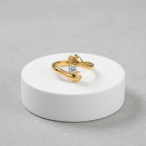 Gold ring with embracing hands design and central diamond.
