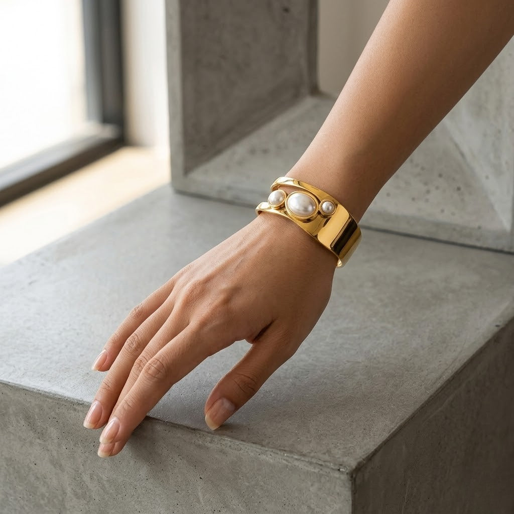 Gold cuff bracelet with pearls worn on a wrist, casual setting, modern style.