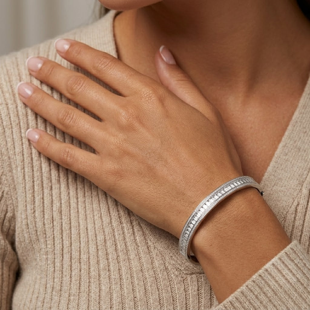 A close-up of a woman wearing a slim silver bangle bracelet with a row of small clear stones, shown against a beige ribbed sweater - J.Collins Jewelry