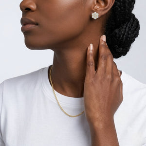 A close-up lifestyle shot of a model wearing a delicate gold chain necklace and a silver-toned flower-shaped stud earring, paired with a white t-shirt against a light gray background. J.Collins Jewelry
