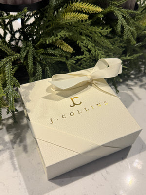 Gift box with a bow and 'J. Collins' branding on a textured surface with greenery.