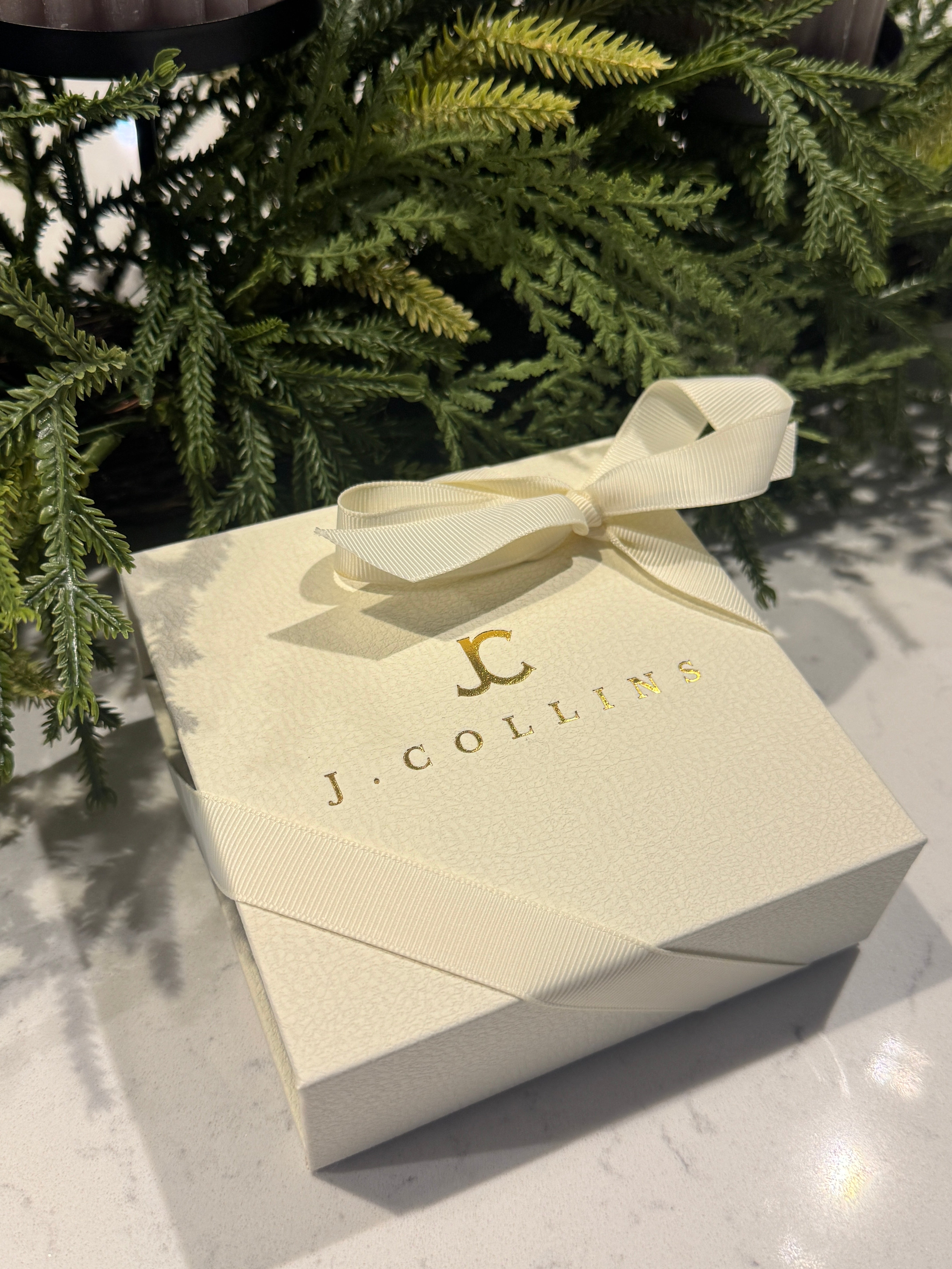 Gift box with a bow and 'J. Collins' branding on a textured surface with greenery.