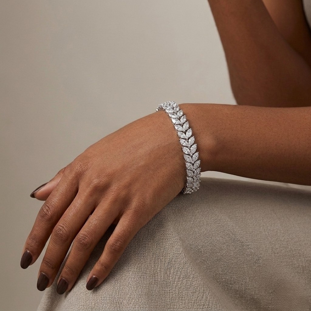 A close-up of a model's hand and wrist wearing a silver-toned leaf-link bracelet adorned with clear pavé stones and a central square diamond cluster, set against a neutral beige background.