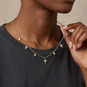 Model wearing a delicate gold dangling cross charm necklace with bezel-set diamond accents | J.Collins Jewelry