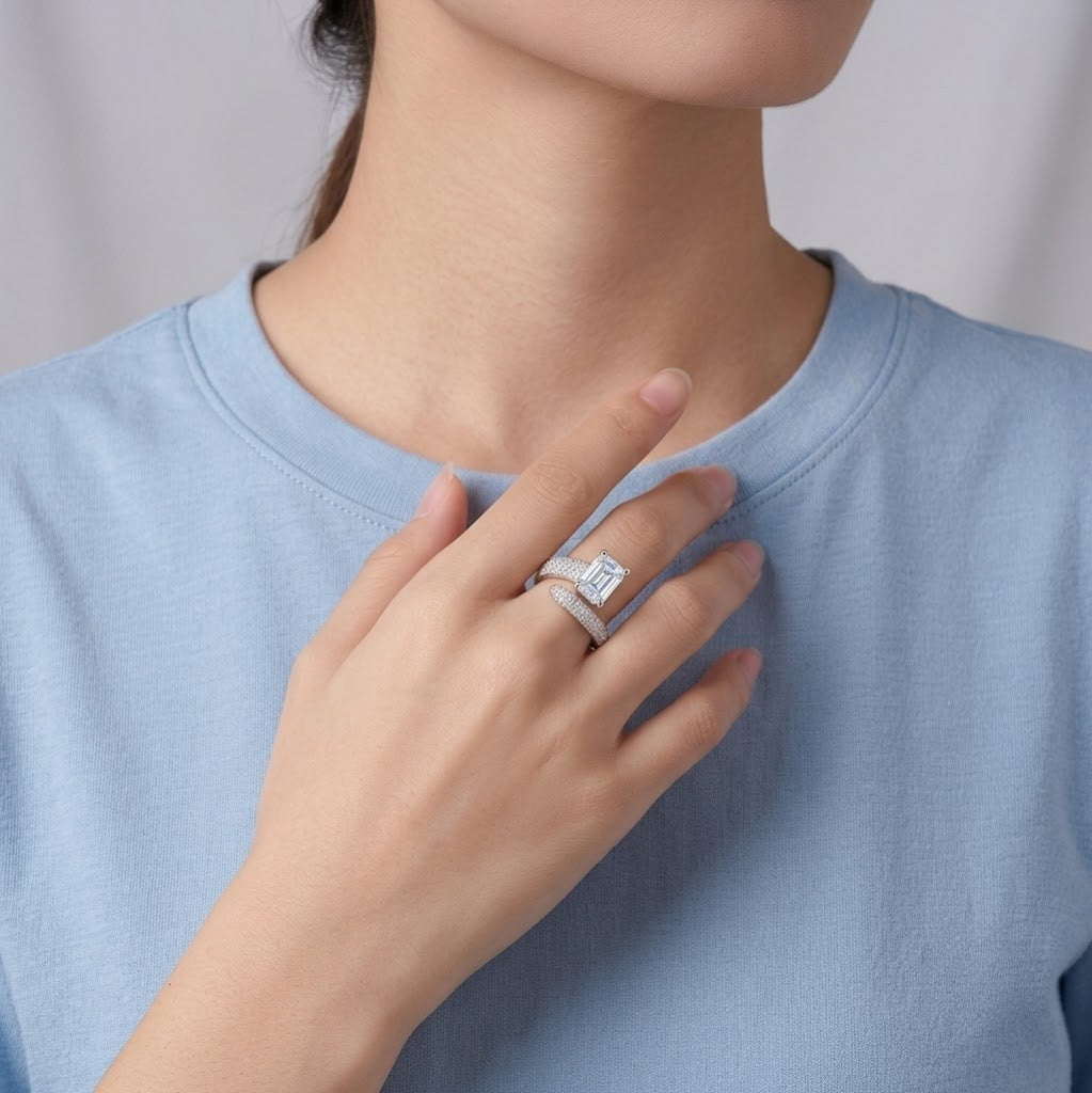 A close-up of a person wearing a silver ring with a square-cut clear gemstone, styled with a matching silver band, while wearing a light blue crewneck t-shirt - J.Collins Jewery