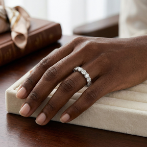 Hand wearing 18K gold lab diamond ring with seven 3.0mm stones on a wooden table near books.