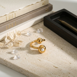 Gold and pearl sphere ring on marble slab with decorative accents and books in the background