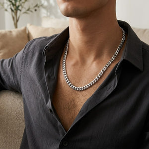 Man wearing silver Miami Cuban Link Necklace 5mm with open black shirt, sitting on a beige couch.