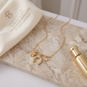 Gold necklace with clover, horseshoe, and diamond charms on a marble surface, elegant and luxurious style