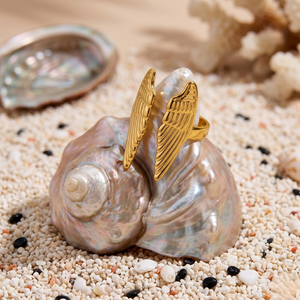 Gold 18K wing loop ring on a seashell with a sandy and coral background.