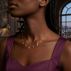 Gold droplet diamond necklace on model wearing purple dress in elegant interior setting