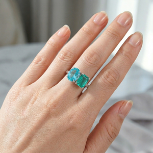 Hand wearing 14K white gold ring with lab emerald and blue gemstone, shown in a natural light setting