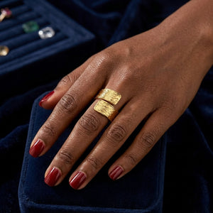 Gold textured coil ring on a model's hand with deep red nail polish, displayed on a dark velvet background.