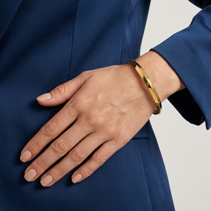 Gold torque cuff bracelet on a wrist, against a blue sleeve background