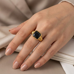Gold signet ring with black stone on person’s hand, displaying elegant style and craftsmanship.