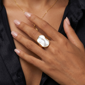 Gold ring with organic-shaped white pearl detail on model's hand wearing a dark blouse