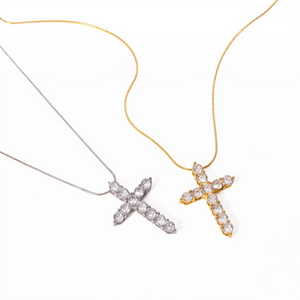 Two cross-shaped pendants; one silver with crystals, one gold with crystals, on thin chains on a white background.