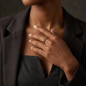 Gold textured linked ring on woman's hand wearing a black outfit, showcasing elegant fashion and style.