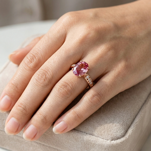 18K rose gold ring with pink gemstone on hand, displayed on a velvet cushion
