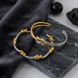 Duet Knot Bangle in silver and gold with knot details, placed on dark marble and velvet background.